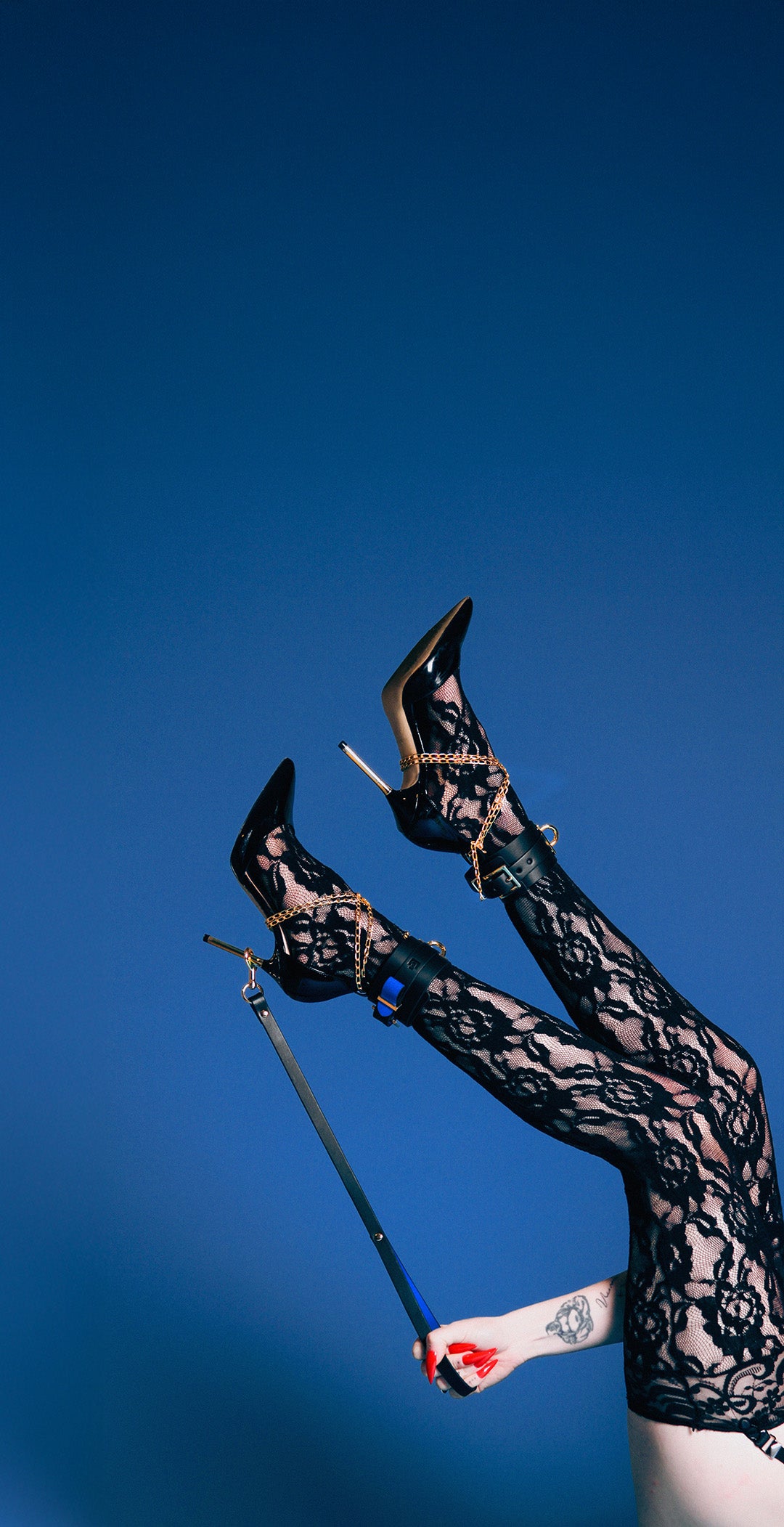 Person wearing high-heeled shoes and a black patterned outfit against a blue sky.